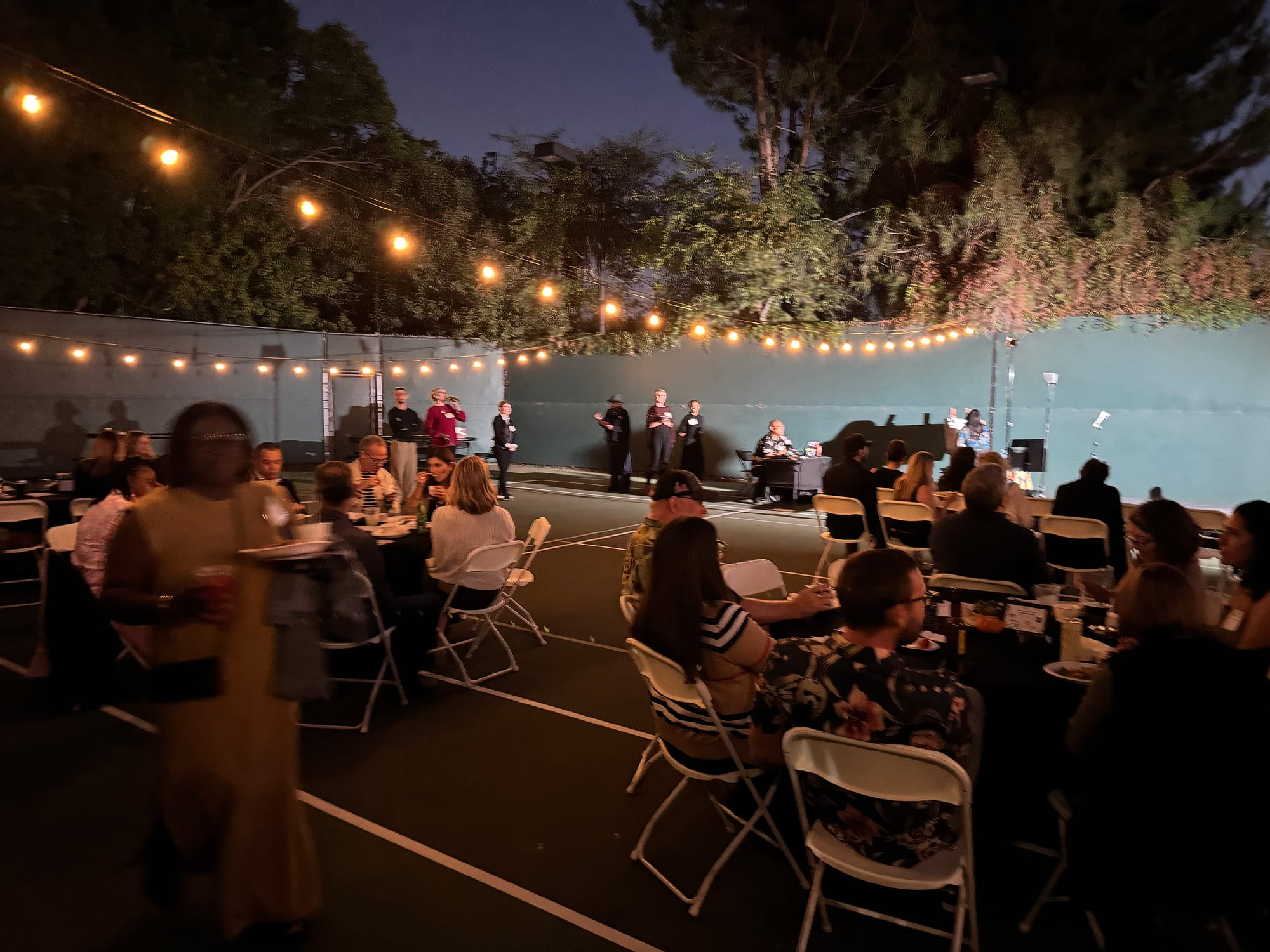 Guests at dinner tables under string lights on the grounds