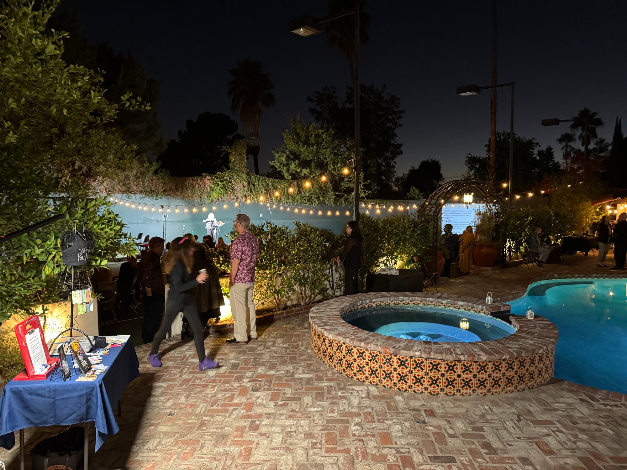 Guests mingling on the brick patio beside the pool at night