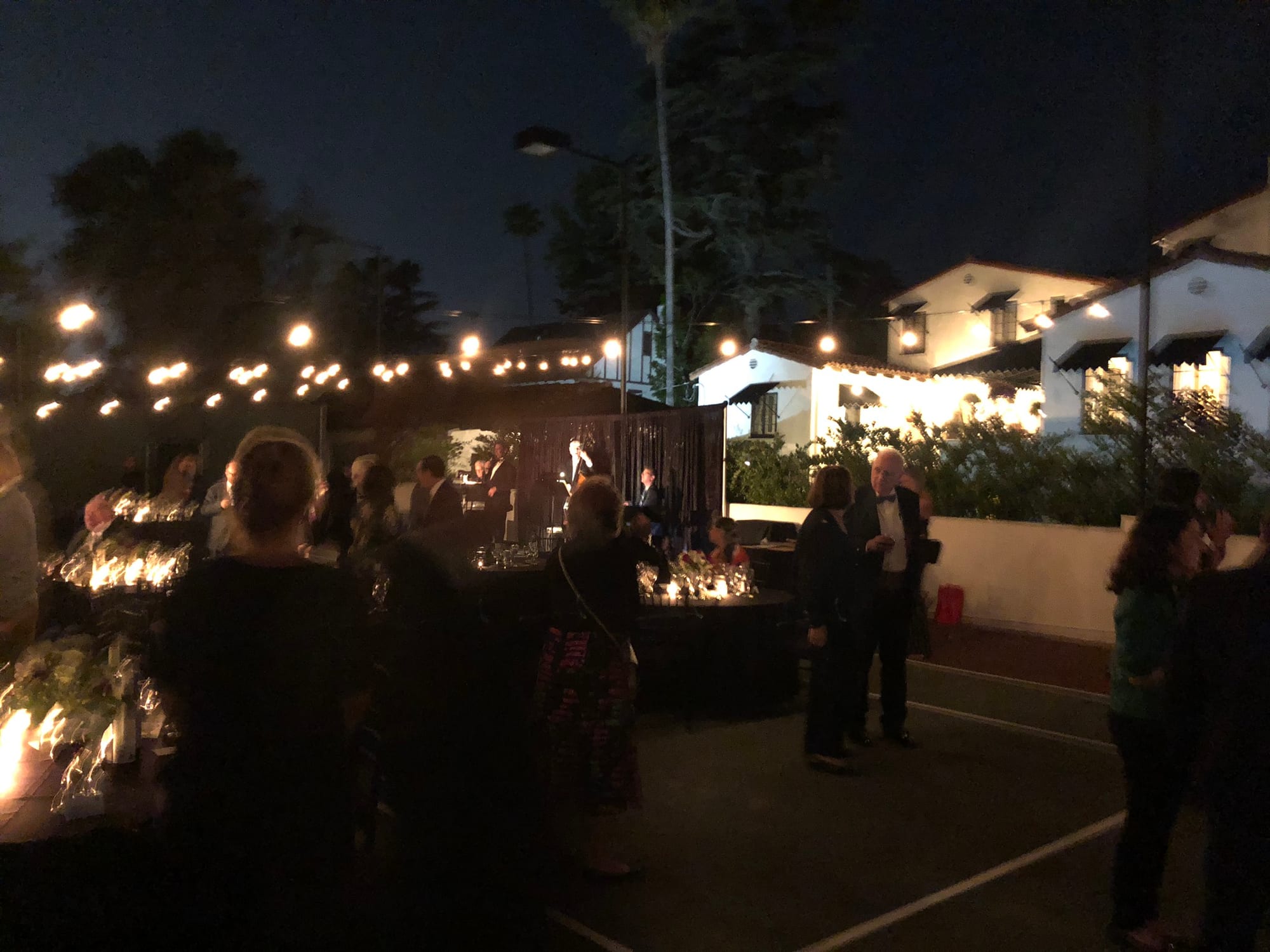 Guests gathering under string lights as dusk falls over the grounds